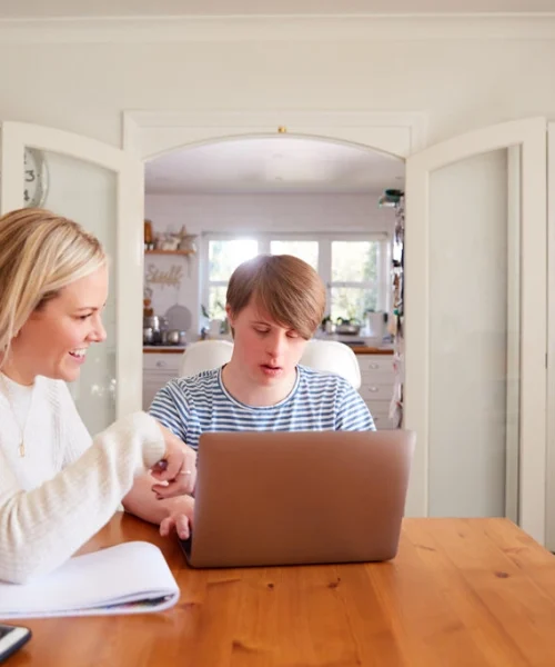 Carer helping disabled boy on laptop in own home