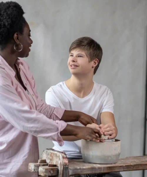 Carer helping disabled boy in art class